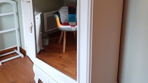 A room with a white wardrobe, a wooden floor, and a chair with a patterned cushion. - Gite Coriosolites (Quemper-Guézennec)