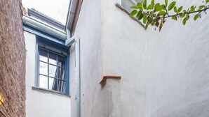 A narrow brick alleyway with a bench, a small garden, and a building with a window and door.