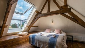 A bedroom with a sloped ceiling, wooden beams, a skylight, a bed with pillows, and a radiator.