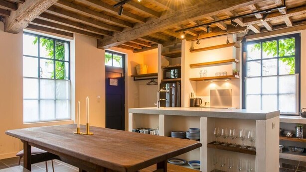 A kitchen with a wooden table, a built-in island with shelves, and a view of greenery outside.