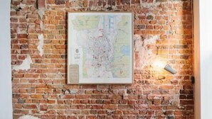 A rustic room with a brick wall, two wicker chairs with fur throws, a map, and a wall-mounted light.