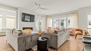 A spacious living room with a fireplace, grey sofas, a round coffee table, and a ceiling fan. - Seashell Serenity Private Pool + Resort Community (Kill Devil Hills)