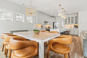 A modern kitchen with white cabinetry, a wooden dining table with leather chairs, and pendant lighting.