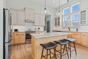 A modern kitchen with white cabinetry, a central island with stools, a stainless steel refrigerator, and pendant lighting.