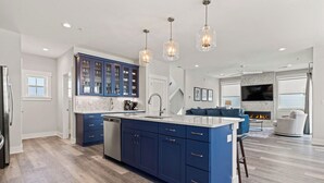 A modern kitchen with blue cabinets, a central island, and pendant lighting. - Lighthouse Loft - Cabana Services + Private Pool (Kill Devil Hills)