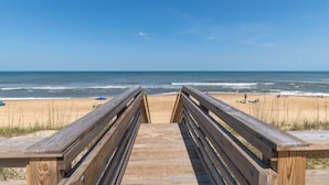 Una pasarela de madera que lleva a una playa con cielos despejados y mar tranquilo.