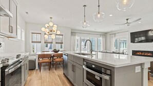 A modern kitchen with a large island, stainless steel appliances, and pendant lighting. - Sunset Soiree - Private Pool + Resort Amenities (Kill Devil Hills)