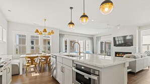 A modern kitchen with a central island, wooden dining table, and pendant lighting.