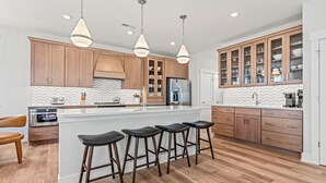 Een moderne keuken met houten kastjes, een groot eiland met barkrukken, roestvrijstalen apparatuur en hanglampen.