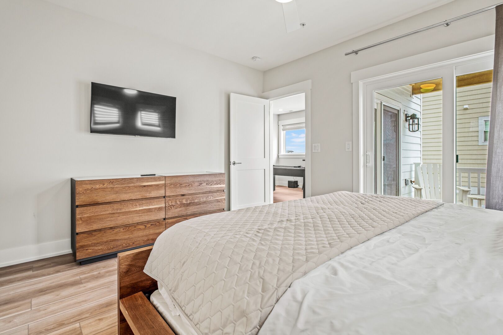 A bedroom with a bed, wooden dresser, and a TV on the wall.