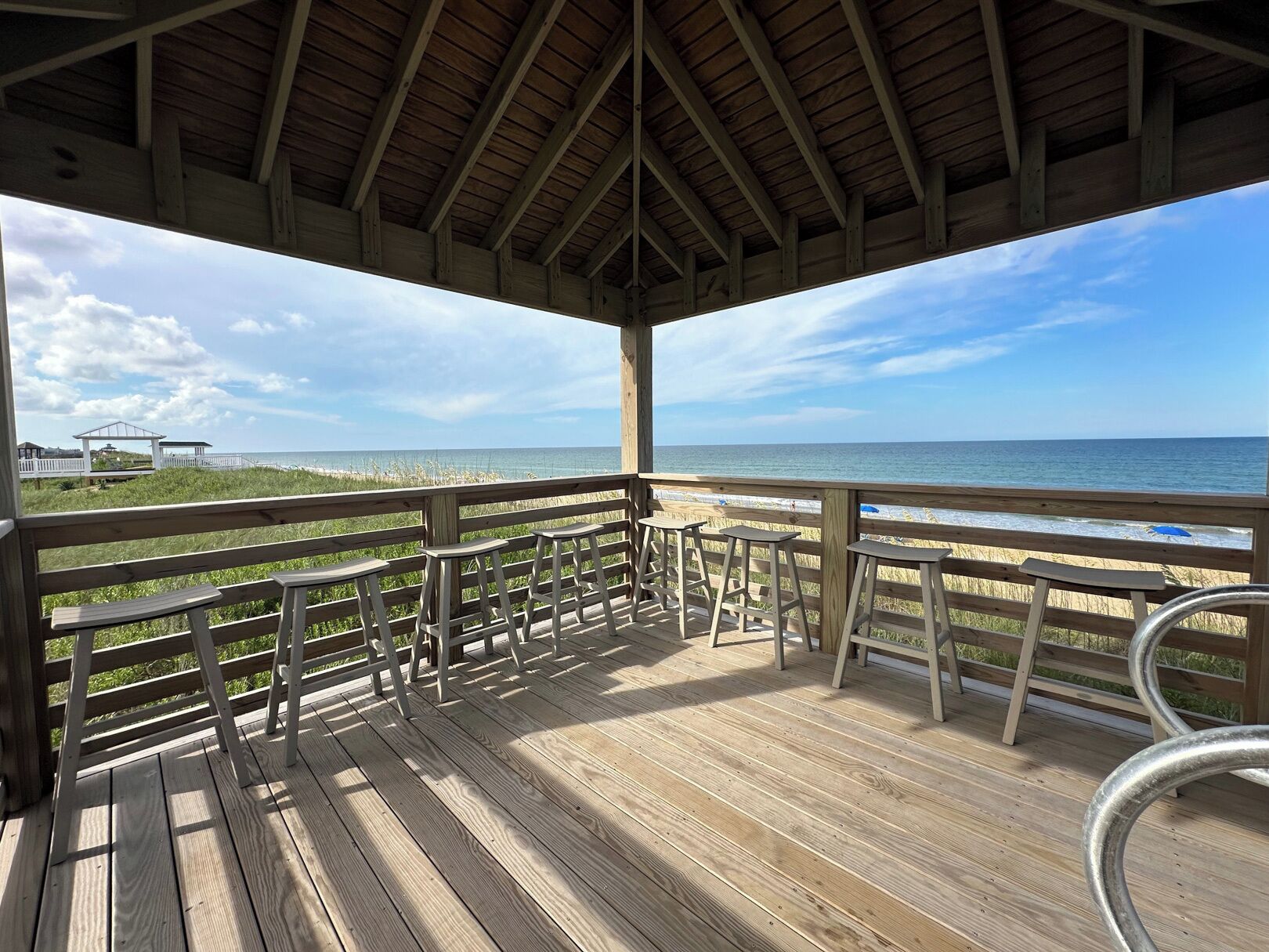 Terraza de madera con barandilla, con vista a la playa y al océano.