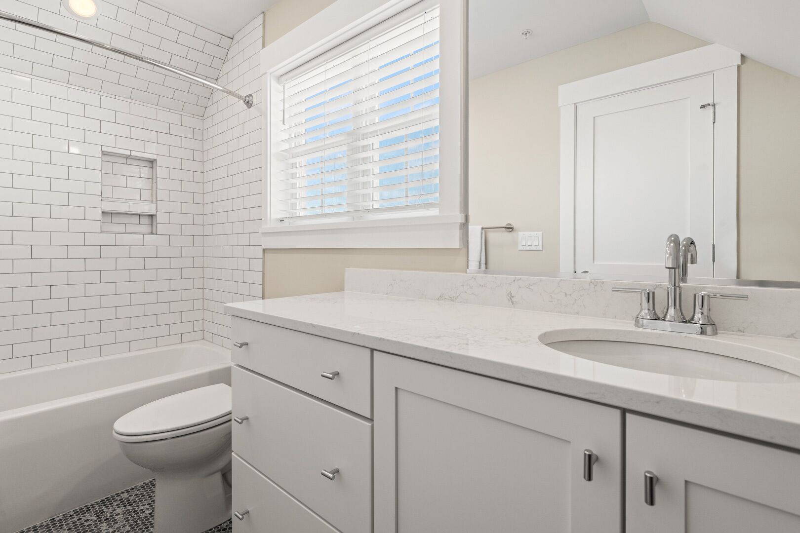 Een moderne badkamer met witte metrotegels, een wit toilet, een marmeren wastafel en een grote spiegel.
