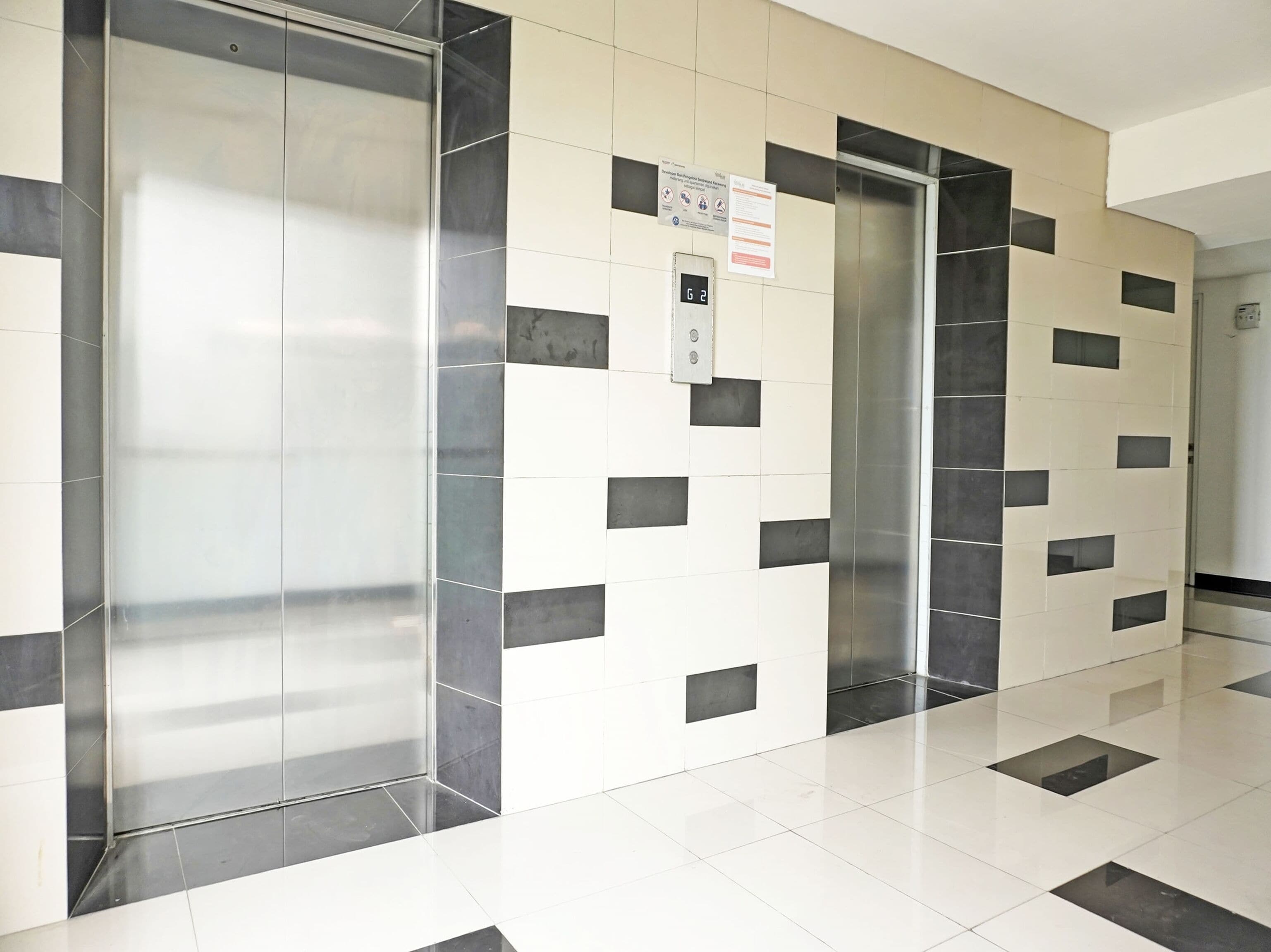 A modern elevator with a digital display, surrounded by a tiled wall with a geometric pattern.