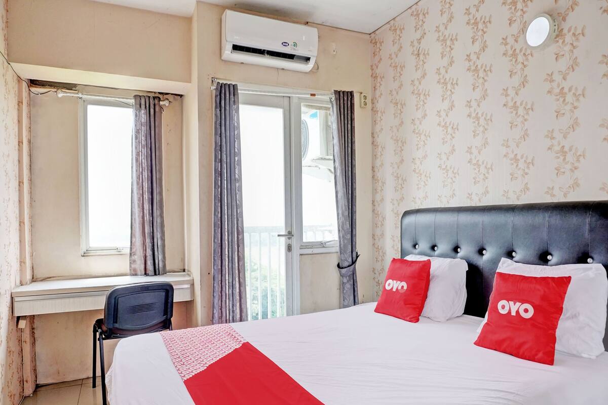 A hotel room with a bed, a desk, and an air conditioning unit.