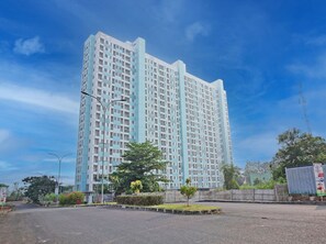 A high-rise building with a modern design, featuring a grid of windows and a prominent central tower. - Collection O 92967 Apartement Sentraland Karawang By Rda Living (Karawang)