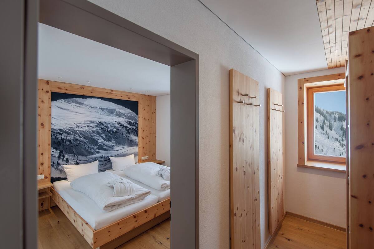 Un dormitorio con una cama grande, paredes de madera, un ventanal con vistas a la montaña y un cuadro de un paisaje nevado.