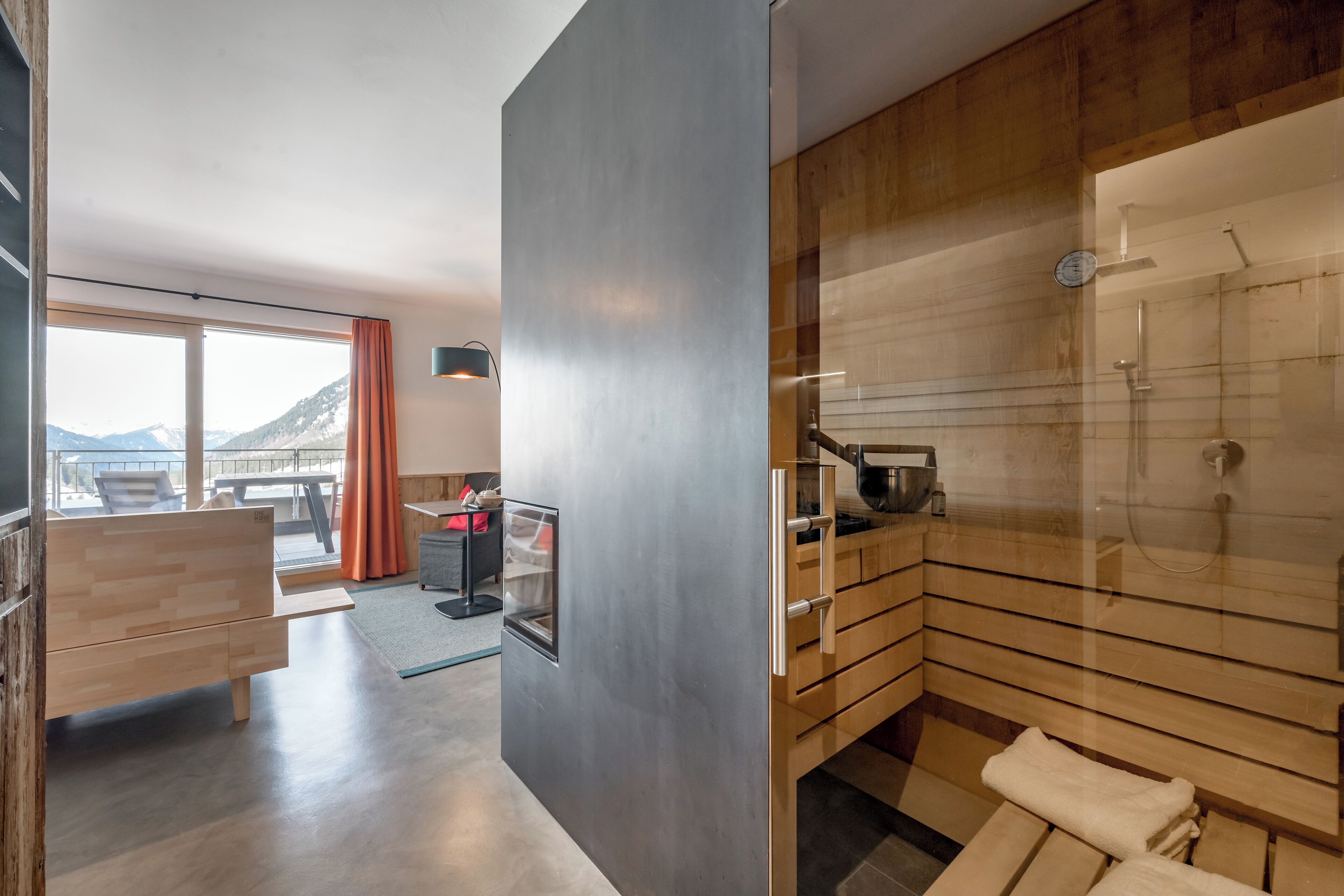 Un baño moderno con cabina de ducha acristalada, muebles de madera y vistas a montañas a través de amplias ventanas.