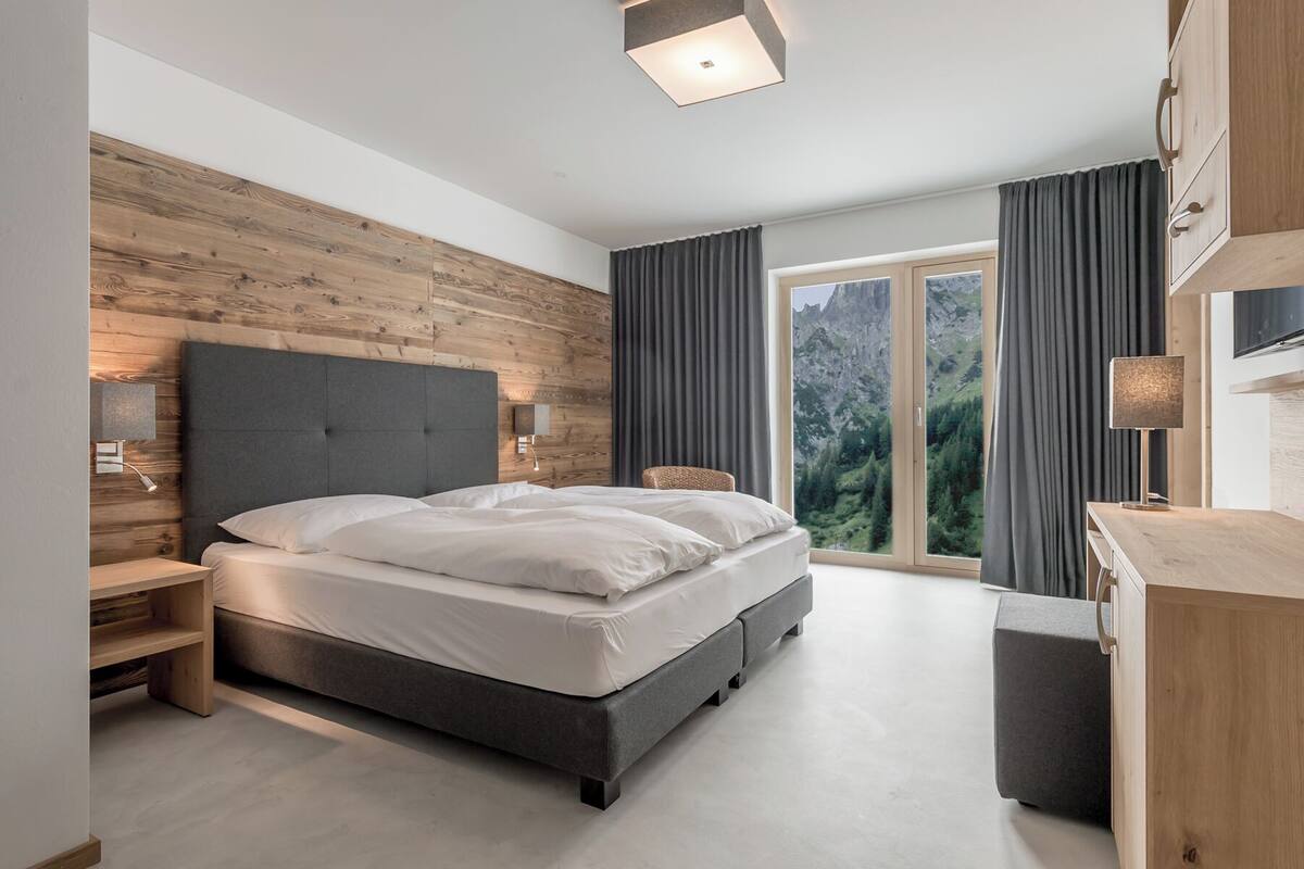 Un dormitorio moderno con una cama grande, paneles de madera, vistas al exterior y un escritorio con lámpara.