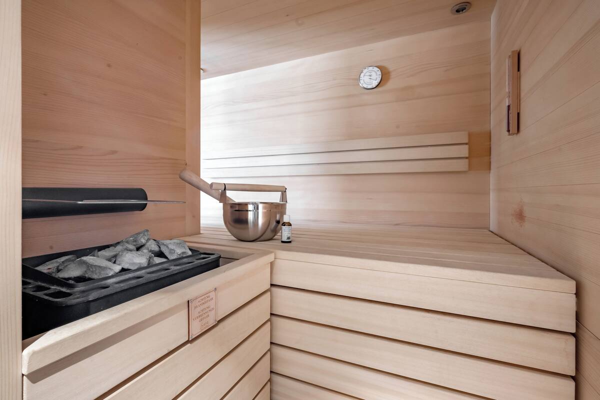 Una sauna con interior de madera, un horno de carbón, un cuenco de metal y una botella pequeña.