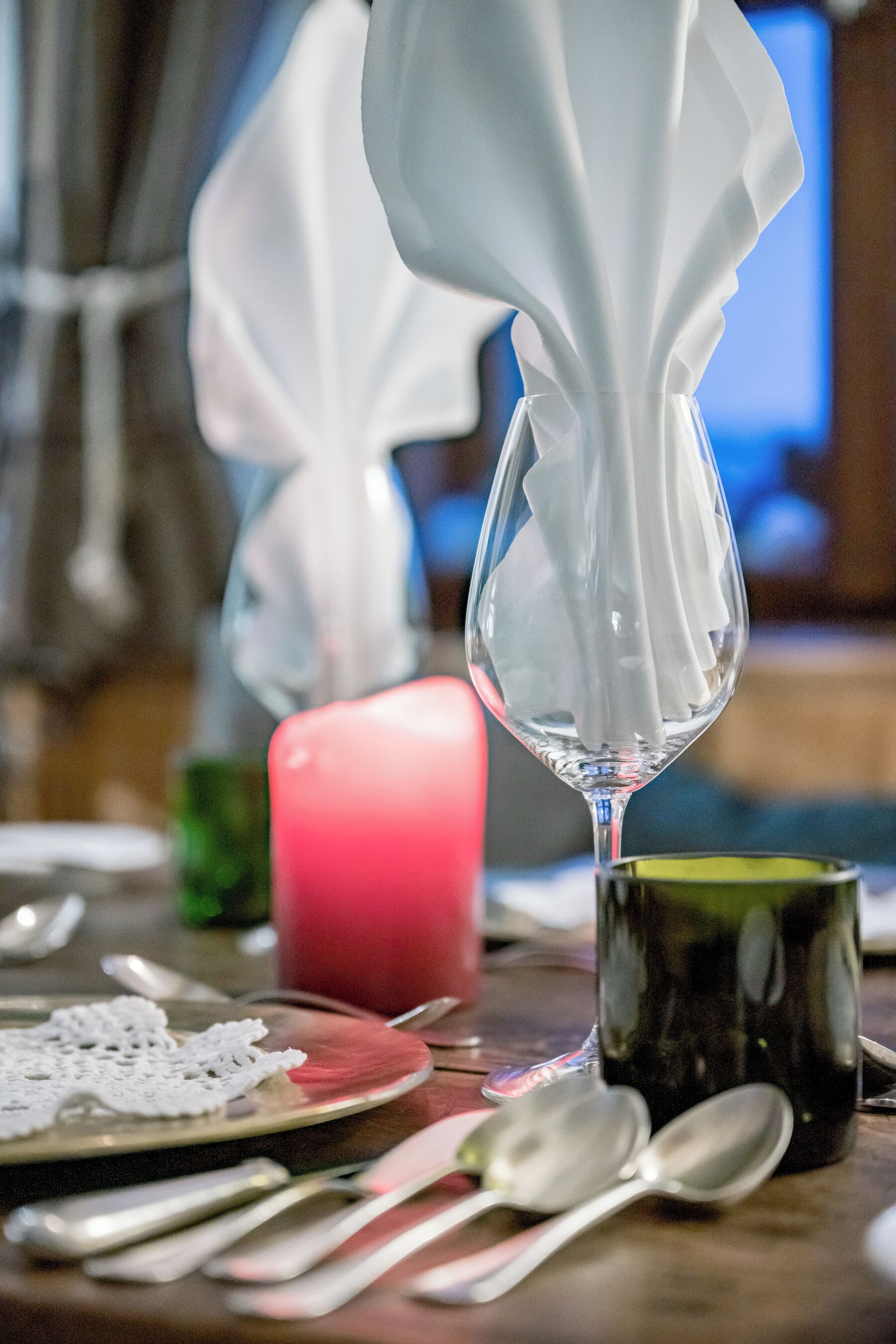 A dining table with a clear glass wine glass, a red candle, and a green mug.