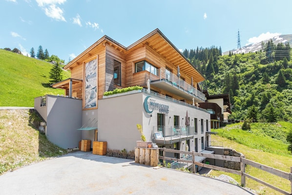 Un hotel moderno con fachada de madera, un balcón y vistas a una ladera verde.