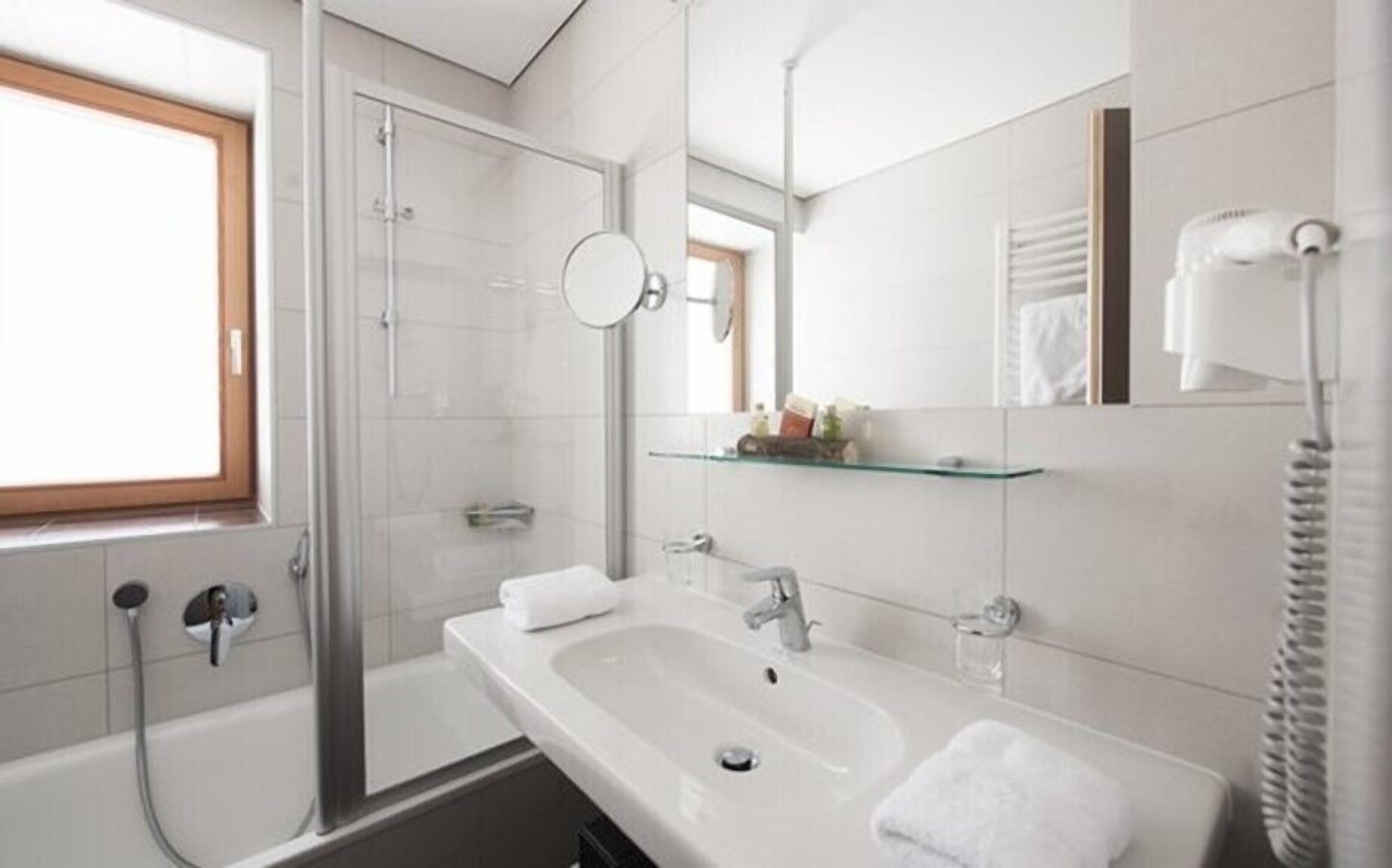 Un baño moderno con cabina de ducha de vidrio, un lavamanos grande con espejo y un perchero para toallas.
