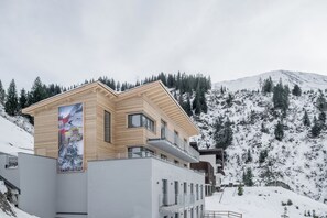 A modern building with a wooden facade and multiple balconies, surrounded by a snowy mountainous landscape.