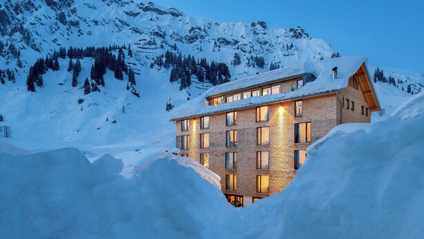 Un chalet de montagne enneigé, doté de nombreuses fenêtres et d’une façade en briques.