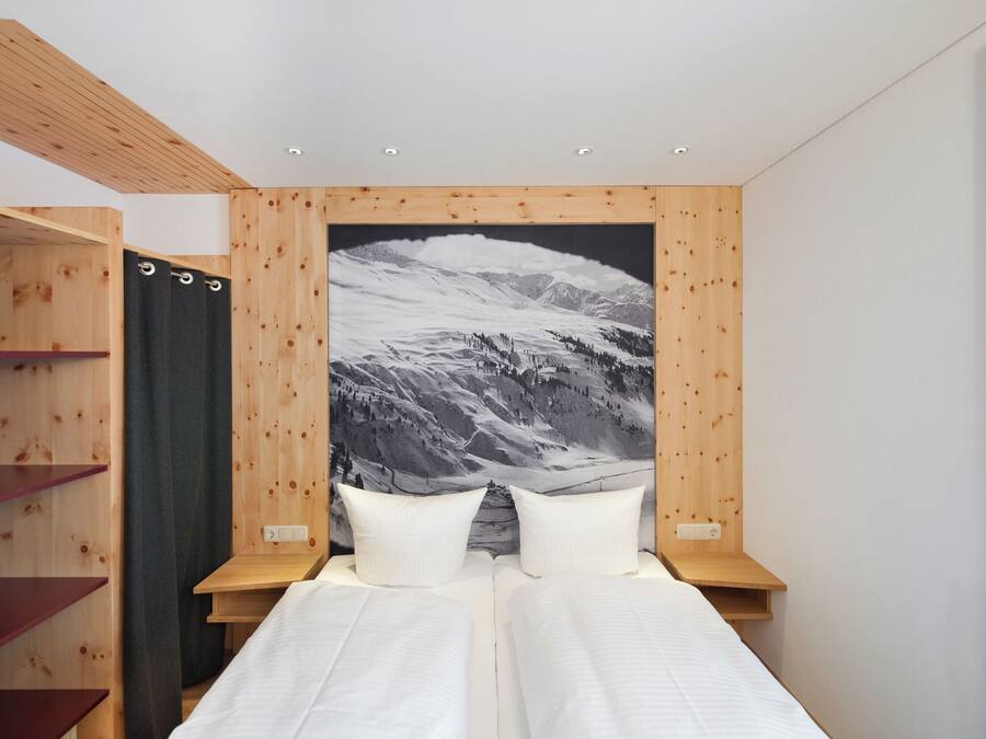 Quarto com cama, cabeceira de madeira e uma grande pintura de paisagem montanhosa.