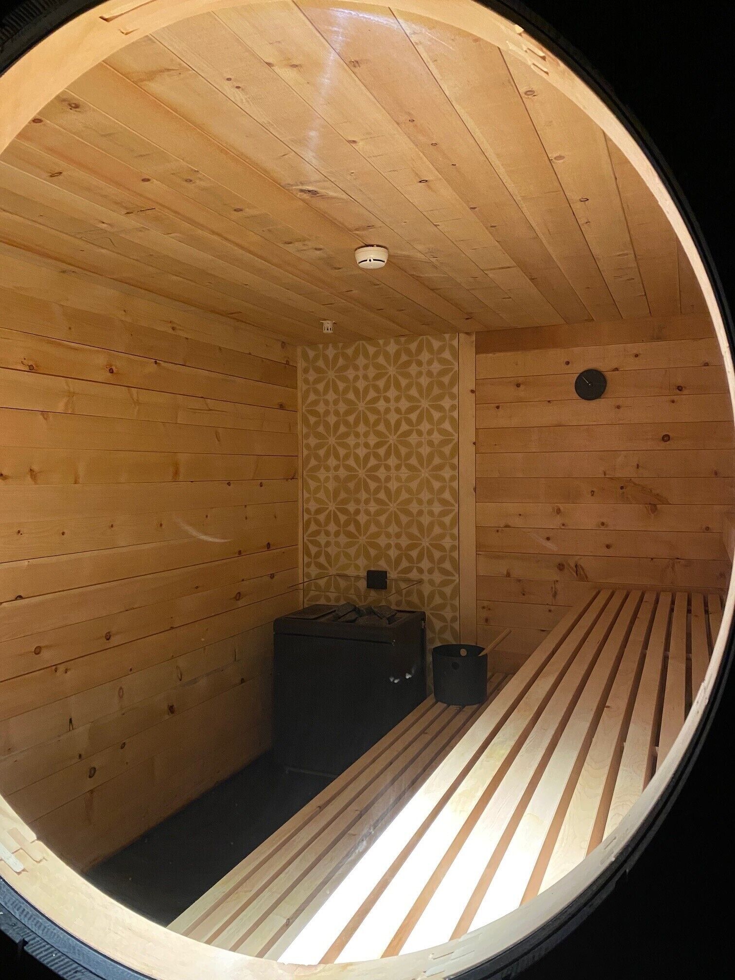 A circular wooden room with a patterned wall, a bed, and a small heater.