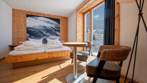 Une chambre à coucher avec un lit en bois, une table ronde, une chaise et une grande fenêtre donnant sur les montagnes.