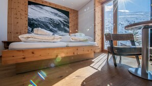 Une pièce avec un mur en bois, une grande fenêtre, un lit avec une literie blanche et une chaise en osier.