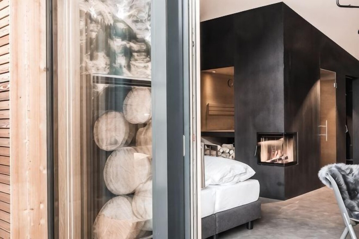Ein modernes Interieur mit Kamin, einem Bett und einer Glaswand mit Holzscheiten.
