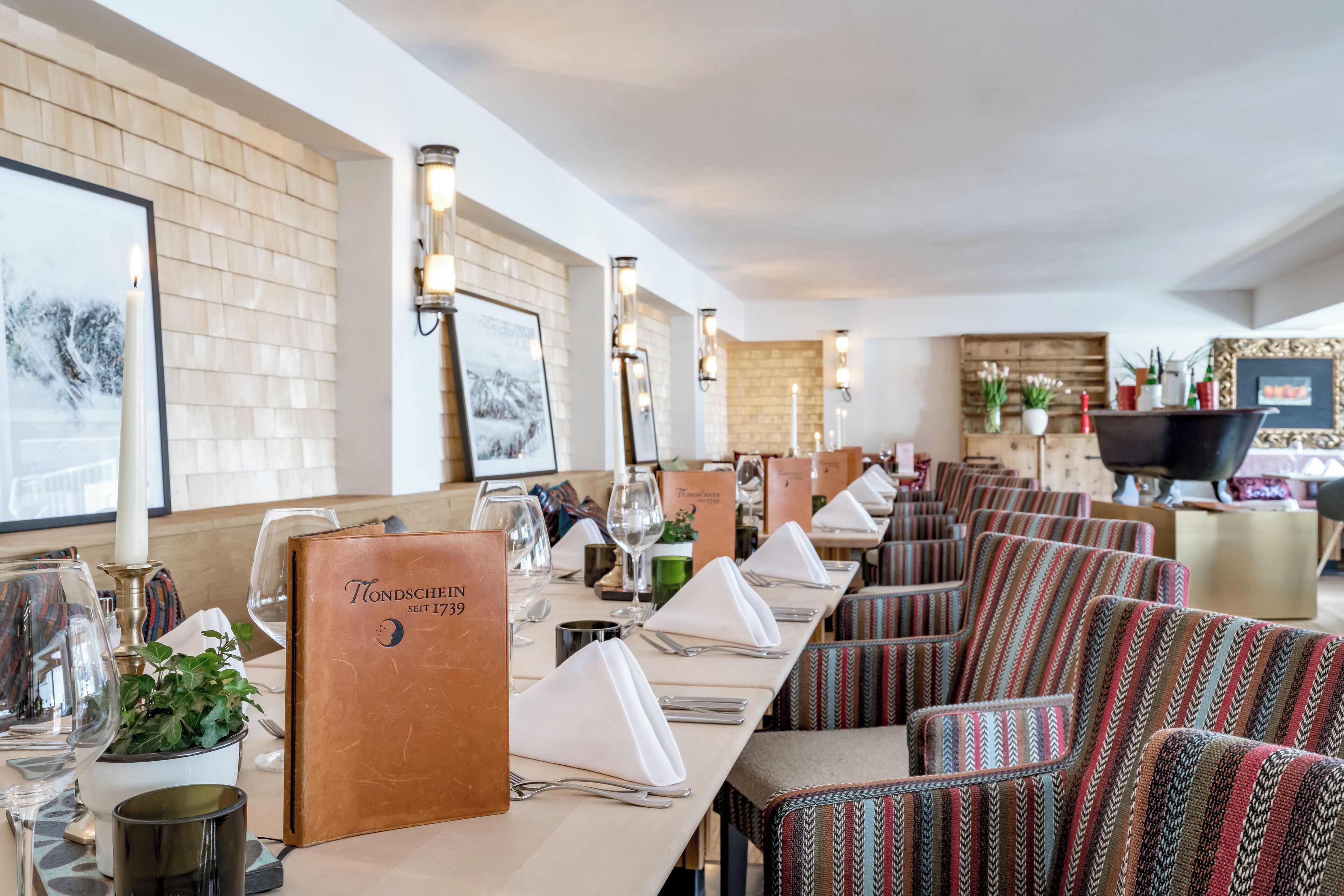 A restaurant with a long table set for a meal, striped chairs, and framed pictures on the wall.