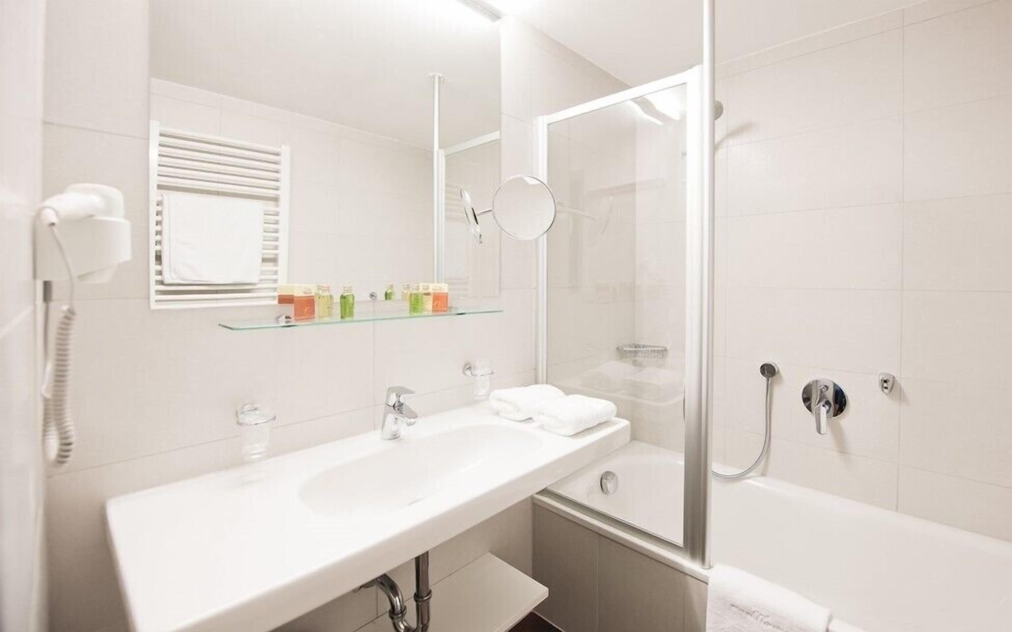 A modern bathroom with a white sink, mirror, and glass shower enclosure.