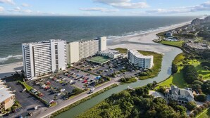 Un hotel costero con varios edificios altos, un estacionamiento y un río que atraviesa la propiedad.