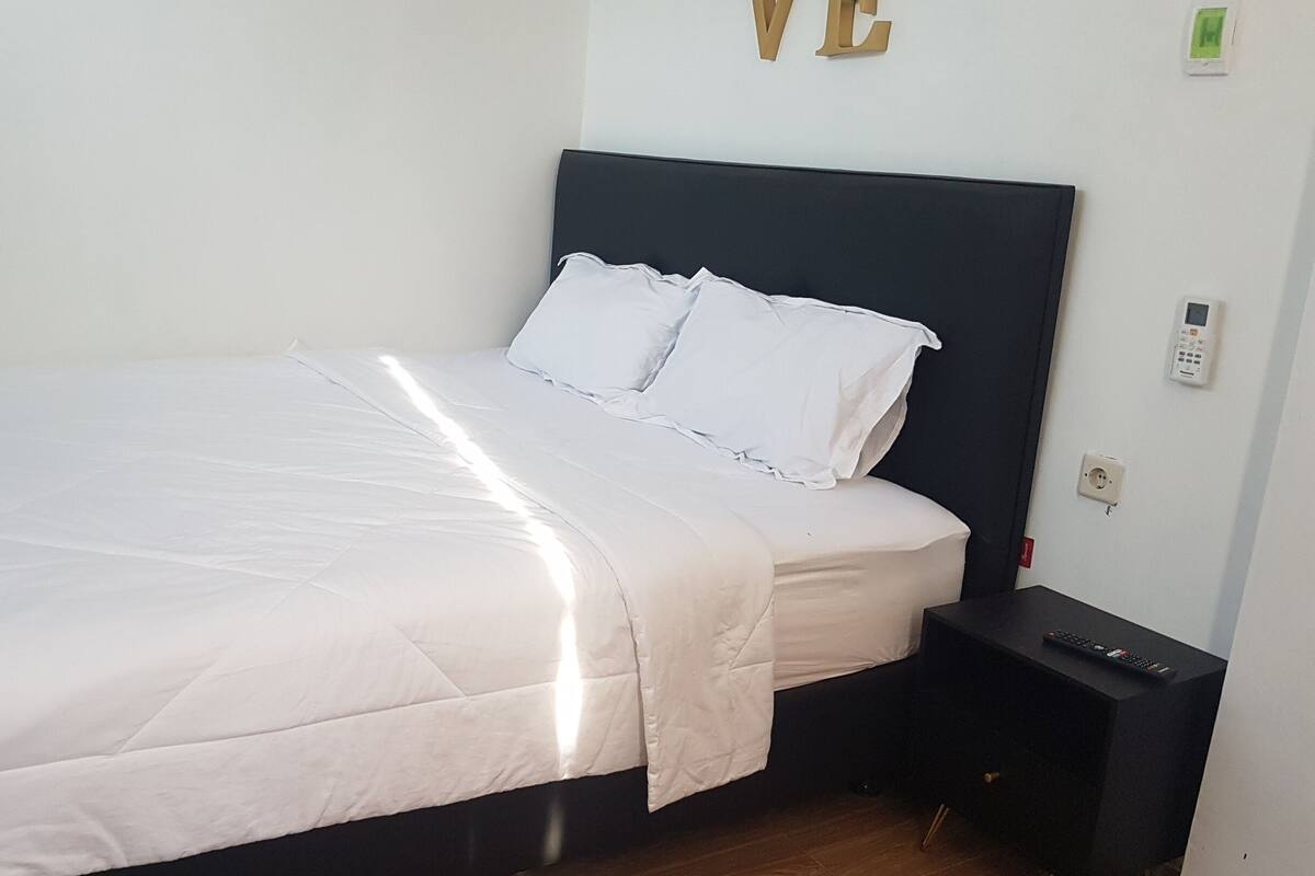 A neatly made bed with white bedding in a room with a dark headboard.