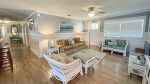 A spacious living room with a beige sofa, white wicker chairs, and a patterned rug. - 2 Bedroom Bay Front Home - Monthly Rentals (Dauphin Island)