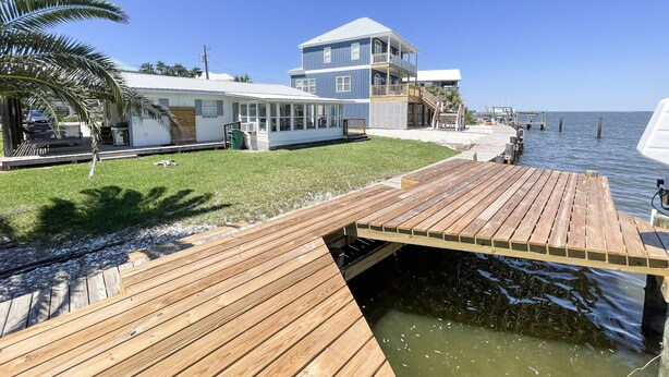 A waterfront property with a wooden deck, a two-story house, and a clear view of the ocean. - 2 Bedroom Bay Front Home - Monthly Rentals (Dauphin Island)