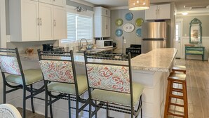 A kitchen with white cabinets, a central island with bar stools, a stainless steel refrigerator, and a hanging light fixture. - 2 Bedroom Bay Front Home - Monthly Rentals (Dauphin Island)