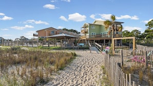 A beachfront property with a sandy walkway, wooden deck, and a two-story building with balconies. - Gulf-view condo steps away from beach! 2 Community Pools!  (Dauphin Island)