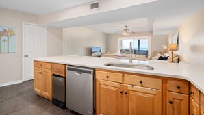 A modern kitchen with wooden cabinets, a dishwasher, and a large island with a sink. - Gulf-view condo steps away from beach! 2 Community Pools!  (Dauphin Island)