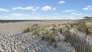 A sandy beach with a wooden fence, a bench, and sparse vegetation. - Gulf-view condo steps away from beach! 2 Community Pools!  (Dauphin Island)