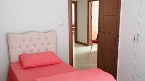 Ein Schlafzimmer mit einem gepolsterten Kopfteil, einem Bett mit rosa Bettwäsche und einem Kleiderschrank.