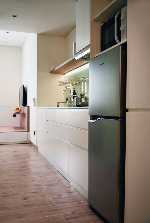 A modern kitchen with a stainless steel refrigerator, white cabinets, and a wooden floor.