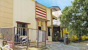 Um edifício com fachada amarela, portão de metal e uma árvore em primeiro plano.
