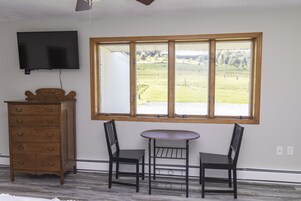Una habitación con un aparador de madera, un televisor montado en la pared y un ventanal con vistas a un campo verde.