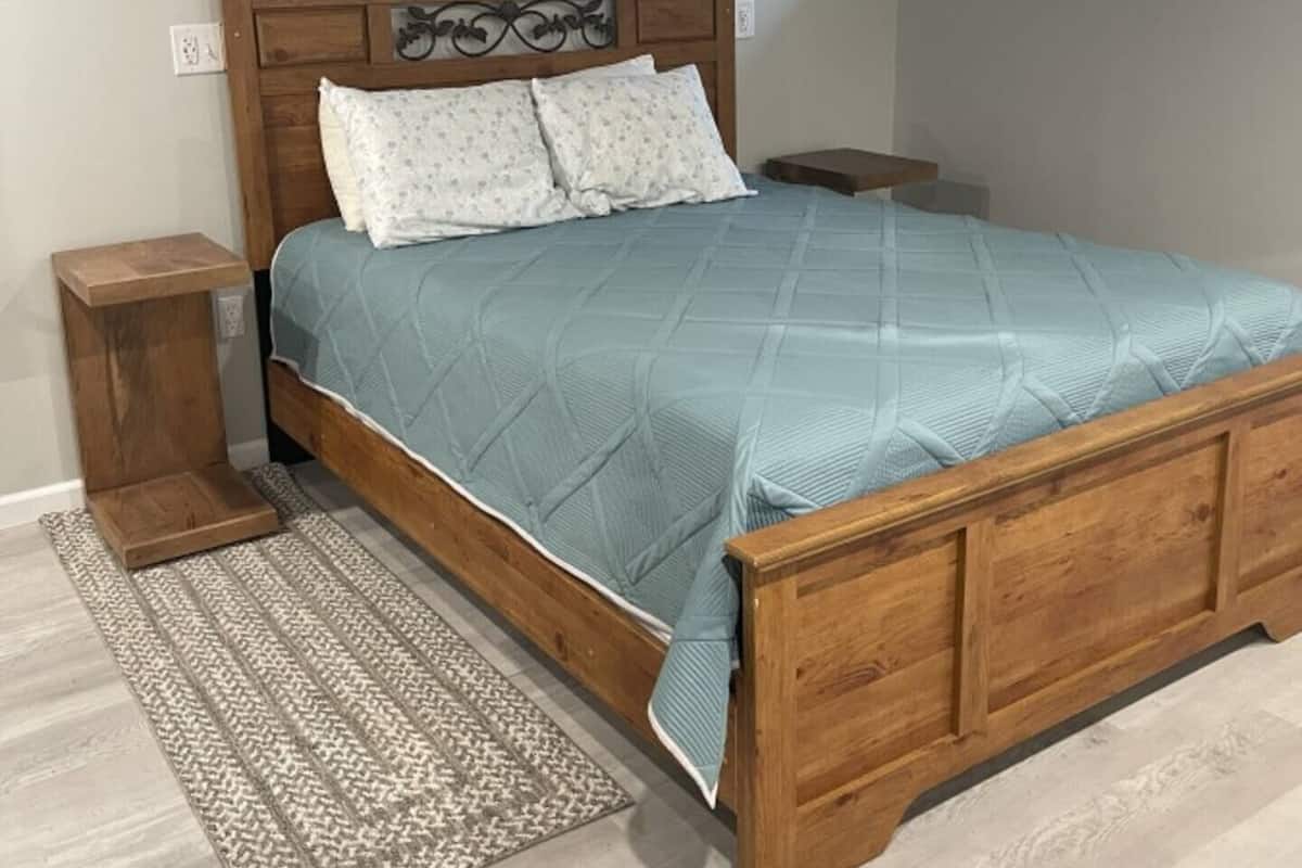 A bedroom with a wooden bed, a bedside table, a rug, and a small window.