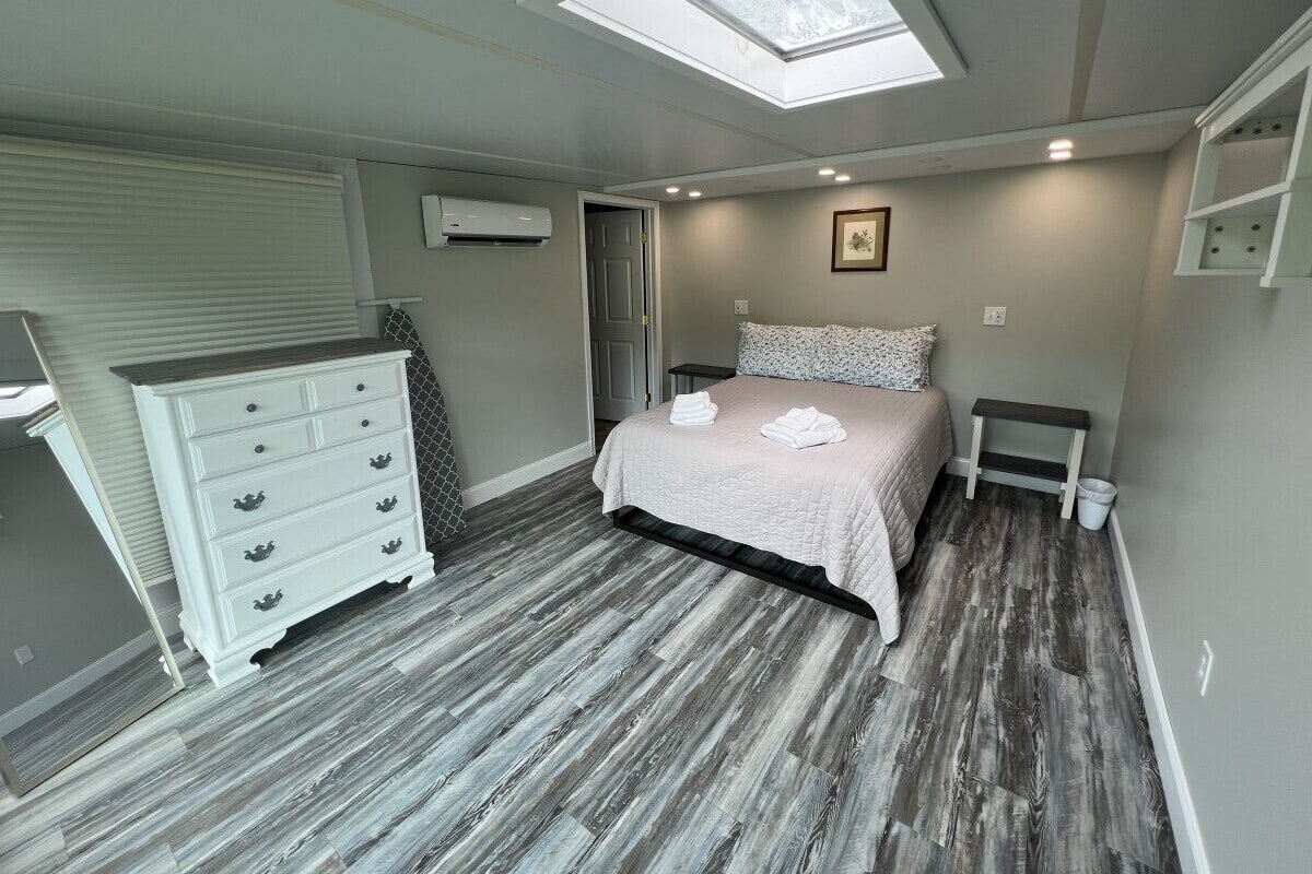 A bedroom with a skylight, a bed with a white comforter, a dresser, and a small bedside table.