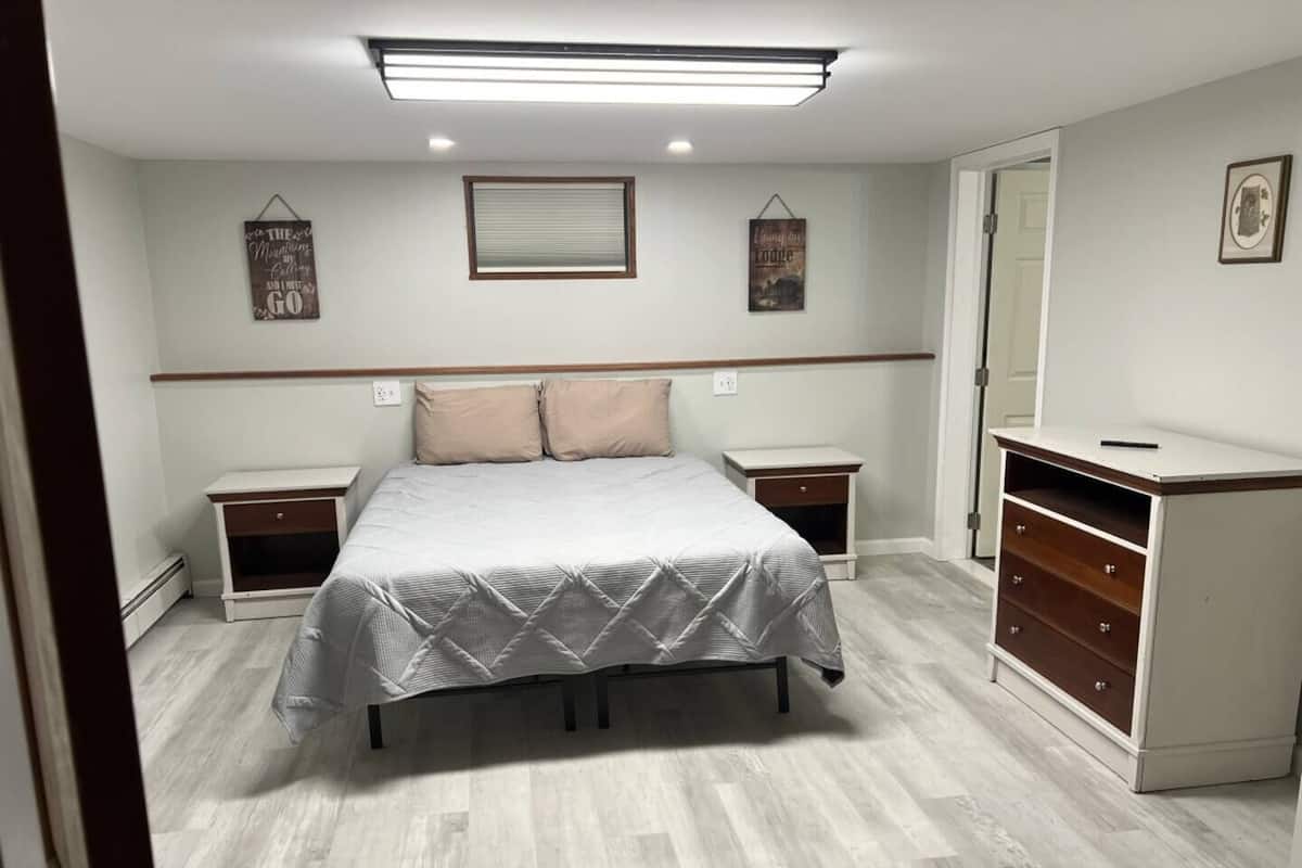 A bedroom with a bed, nightstands, a dresser, and a window with blinds.